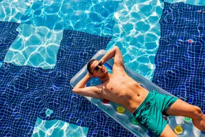 Man in sunglasses relaxing on inflatable raft in the swimming pool on a hot sunny summer day, high angle view
