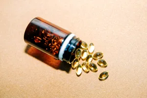 Fish oil, vitamin d, omega 3 capsules are spilling from brown plastic bottle on beige background Fish oil, vitamin d, omega 3 capsules are spilling from brown plastic bottle on beige background