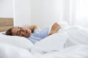 Sleeping woman in blue pajamas in her bed with white duvets. The first hours of nightly sleep are perhaps the most important. Getty Images