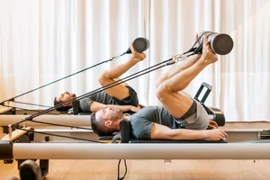 Strong men performing pilates hip mobility exercise on reformer Side view of concentrated male athletes in sportswear performing pilates hip mobility exercise on reformer during workout