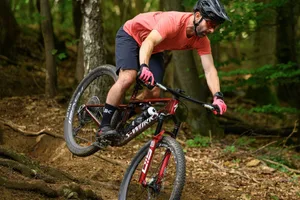 Specialized S Works Epic 9 ride 6 Rider in red t-shirt dropping down over a root spread aboard the Specialized S-Works Epic 9.