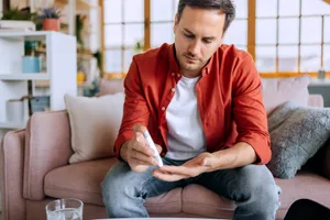 Man checking blood sugar level at home Young man sitting at home using a glucose meter to monitor his blood sugar level, maintaining his daily health routine