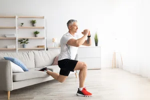 Active mature man doing squats while training at home, doing exercises near sofa in living room interior Active mature man doing squats while training at home, doing exercises near sofa in living room interior, keeping fit during covid-19 quarantine, empty space