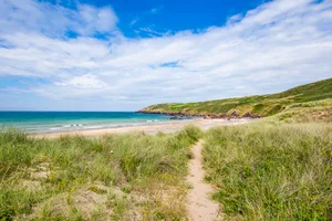Path leading to scenic beach on sand dunes covered with patches of grass in Freshwater West on beautiful Pembrokeshire coast,South Wales,Uk.Beautiful weather, turquoise sea and blue sky with few clouds in background. Beautiful scenery of Pembrokeshire coastline,South Wales, Uk in summer.Scenic landscape of british coast.Path leading to paradise beach trough sandy dunes.Fantastic weather conditions.Turquoise sea and blue sky with few clouds above green cliffs.Shore of Great Britain.