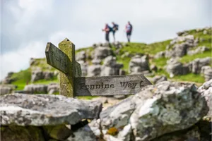 pennine-way A sign for the Pennine Way with distant hikers blurred in the background near Malham Cove in the Yorkshire Dales National Park.