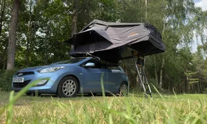 Blue car parked on grass with a black tent on the roof with a ladder coming down Blue car parked on grass with a black tent on the roof with a ladder coming down