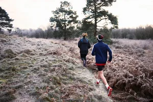 Rear view of mother and son running on frosty grassland