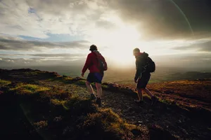 02-174918-offas-dyke-path-pencloddiau-denbighshire Two male hikers on a rugged hill backlit by evening sun