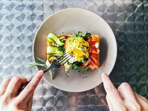 Eating brunch with waffle, avocado, cucumber, salmon and poached egg, personal perspective Eating brunch with waffle, avocado, cucumber, salmon and poached egg, personal perspective