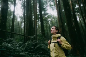 Woman contemplating in forest Woman hiking through a forest in a light yellow coat