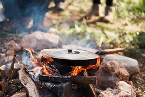 Pan placed on bonfire in nature Camp metal pan placed on bonfire with hot burning firewood with crop tourists of bushcraft tour in nature