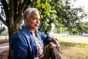 Senior woman leaning on fence and looking out over farm pasture An older woman leans on a fence looking out over a field.