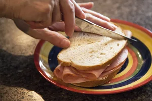 cutting-a-sandwich A hand holding a knife cutting a ham sandwich.