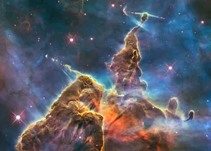 Hubble captures view of “Mystic Mountain” Hubble image of a tall, mountain‑like column of gas and dust with rough, sculpted edges glowing in blue and orange light, surrounded by stars in deep space.