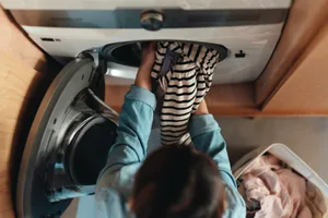 washing-machine-temperature Top view of a person loading a washing machine with dirty clothes