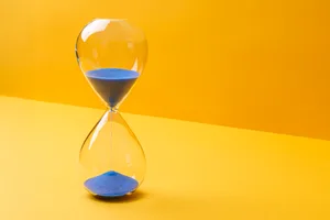 Blue Colored Sand Hourglass On Yellow Background Front view of blue colored sand hourglass on yellow background