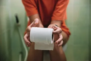 what-is-pee Photo of a person sat on the toilet, focus on the toilet roll in their hands in the foreground