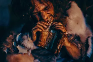 Close-up Portrait of Tribe Leader Wearing Animal Skin Eating in a Dark Scary Cave at Night. Neanderthal or Homo Sapiens Family Cooking Animal Meat over Bonfire and then Eating it. Close-up Portrait of Tribe Leader Wearing Animal Skin Eating in a Dark Scary Cave at Night