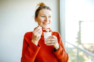 Woman with granola A woman in an orange sweater eating granola and smiling while sun streams through a window