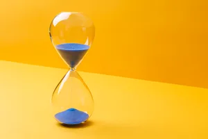 Blue Colored Sand Hourglass On Yellow Background Blue Colored Sand Hourglass On Yellow Background