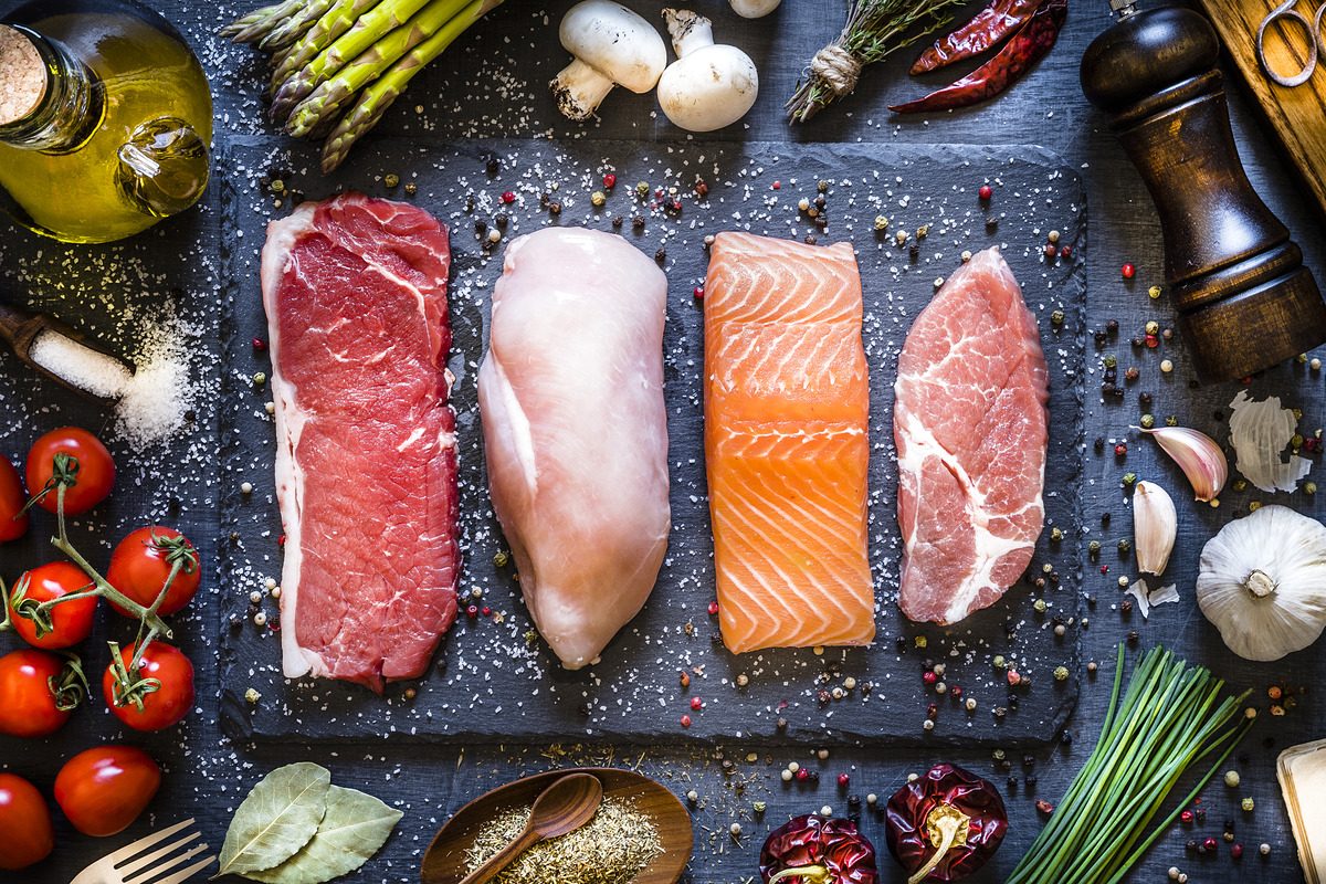 Cuts of raw meat and fish lined up on a slate serving platter