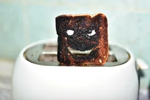 burnt-toast-health Photo of a slice of burnt toast atop a toaster. The toast has a malicious-looking grin carved out of it