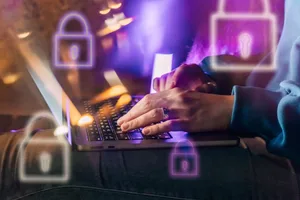 cybersecurity-laptop Female hands typing on a laptop in neon light. A lock as a symbol of cybersecurity on a foreground.