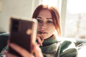 AI-girlfriends Woman with red hair looking on screen of her mobile phone