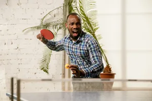 intermediate-skill-plateau Young man playing table tennis in workplace, having fun