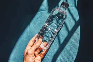 water-bottle-hot A hand grips a water bottle firmly against a backdrop of blue fabric, with natural light highlighting the bottle's transparency
