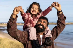 fatherhood-health-conception A waist-up shot of a father carrying his young daughter on his shoulders as they walk along the coast on a beautiful, sunny day. They are both smiling, enjoying their time together by the ocean
