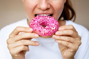 Close-up of a woman eating a donut with pink glaze. Close-up of a woman eating a donut with pink glaze.