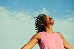 A woman stands with her arms open and eyes closed against a blue sky A woman stands with her arms open and eyes closed against a blue sky