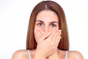 Ozempic breath A close-up of a woman covering her mouth with her hands in front of a white background