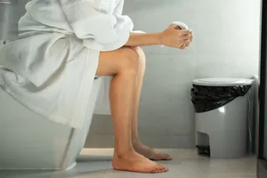 A woman sitting on the toilet in a bathroom holding a roll of toilet paper A woman sitting on the toilet in a bathroom holding a roll of toilet paper