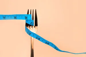 A blue measuring tape wrapped around a fork against a beige background A blue measuring tape wrapped around a fork against a beige background