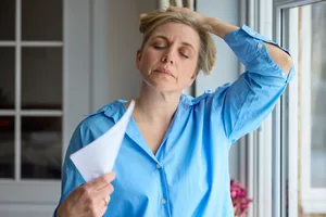 A woman experiencing a hot flush due to menopause fans herself with a piece of paper A woman experiencing a hot flush due to menopause fans herself with a piece of paper