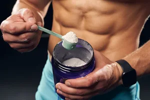Dry scooping A man holding a tub of pre-workout powder in one hand and a scoop in the other