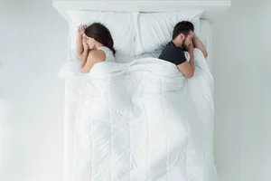What side to sleep on A man and a woman are sleeping back-to-back in a bed with white bedding.