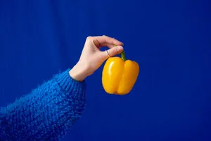 Histamine intolerance A hand holding up a yellow pepper against a blue backdrop