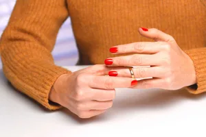 Menodivorce A woman with red-painted nails is removing her wedding ring