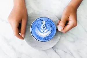 Blue matcha Female hands hold a blue matcha featuring latte art on a marble surface
