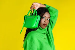 A model wearing a bright green jumper holds a matching green handbag next to her face, in front of a yellow background A model wearing a bright green jumper holds a matching green handbag next to her face, in front of a yellow background
