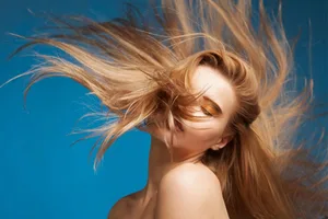 A woman swishing her hair against a blue background A woman swishing her hair against a blue background