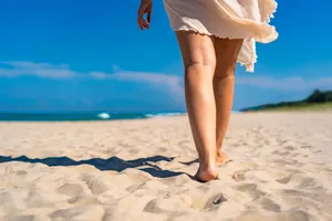 Beautiful mature woman walking on sunny sandy paradise beach in summertime. Back view, close-up for legs Beautiful mature woman walking on sunny sandy paradise beach in summertime. Back view, close-up for legs