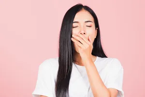 Chronic tiredness Woman yawning against a pink background