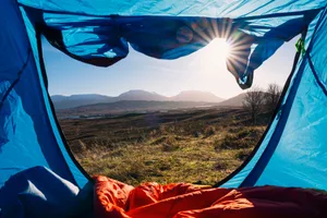Biggest camping mistakes Sun streams into an open tent, which looks out on a beautiful landscape