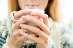 An extreme close-up of a woman holding a steaming drink An extreme close-up of a woman holding a steaming drink