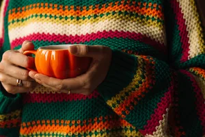 Hands holding orange mug against colorful knit sweater, close up