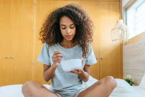 Foods to improve sleep A woman sitting on a bed eating from a bowl